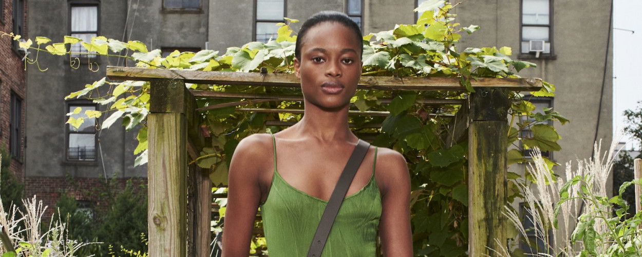 Frau in einem grünen, sommerlichen Viskosekleid steht in einem urbanen Garten mit Holzbogen und Rankpflanzen