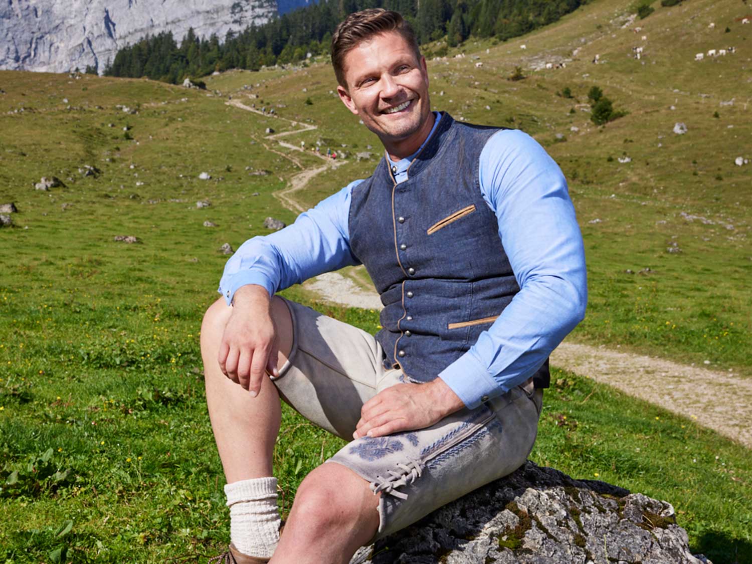 trachtenmode-herrentrachten-trachten-lederhose-herren-trachtenhemd Trachtenfest Mann in Tracht sitzt auf Felsen