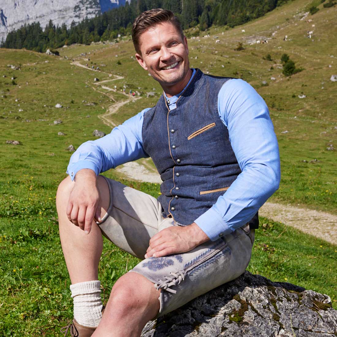 Trachtenfest Mann in Tracht sitzt auf Felsen