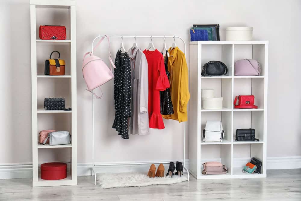 Offene Garderobe mit weißen Regalen voller Handtaschen, Kleiderstange mit bunten Kleidern und ordentlich arrangierten Schuhen auf dem Boden Offene Garderobe mit weißen Regalen voller Handtaschen, Kleiderstange mit bunten Kleidern und ordentlich arrangierten Schuhen auf dem Boden